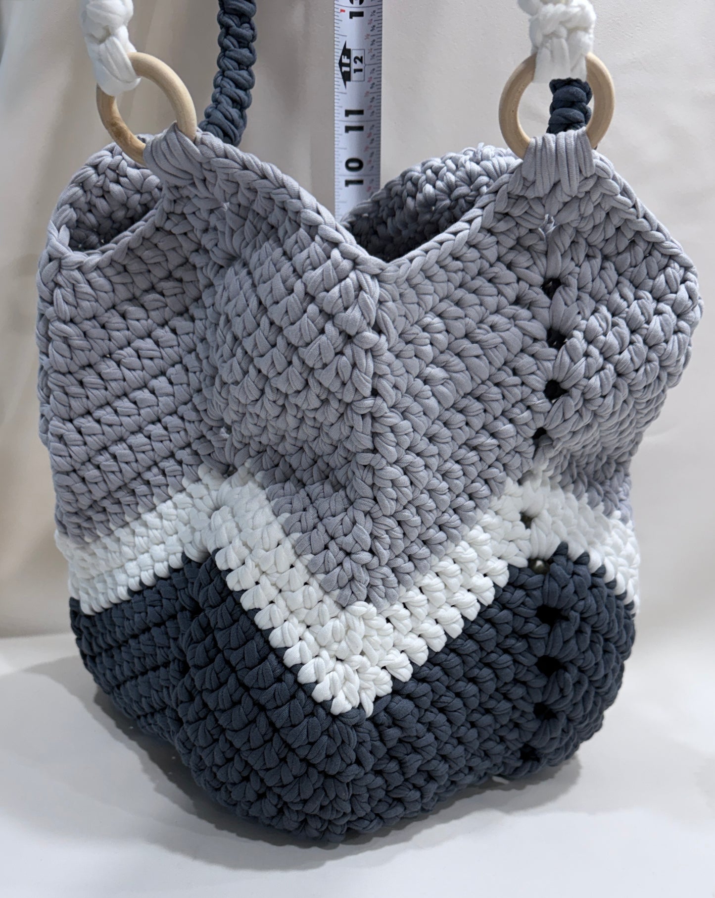 Crocheted bag with gray, white, and dark gray stripes on a light background