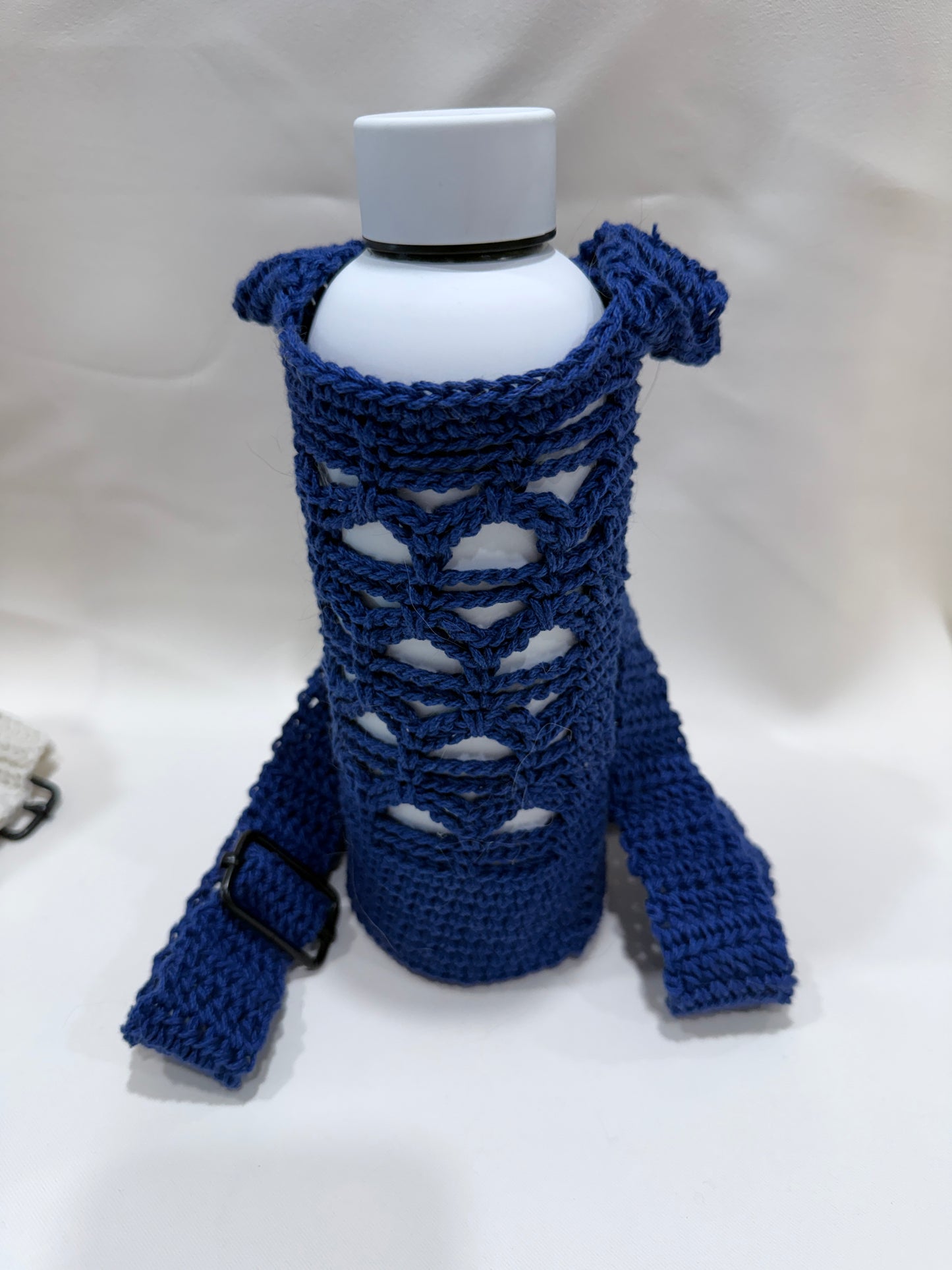 Blue crocheted water bottle holder with a crossbody adjustable strap holding a white bottle