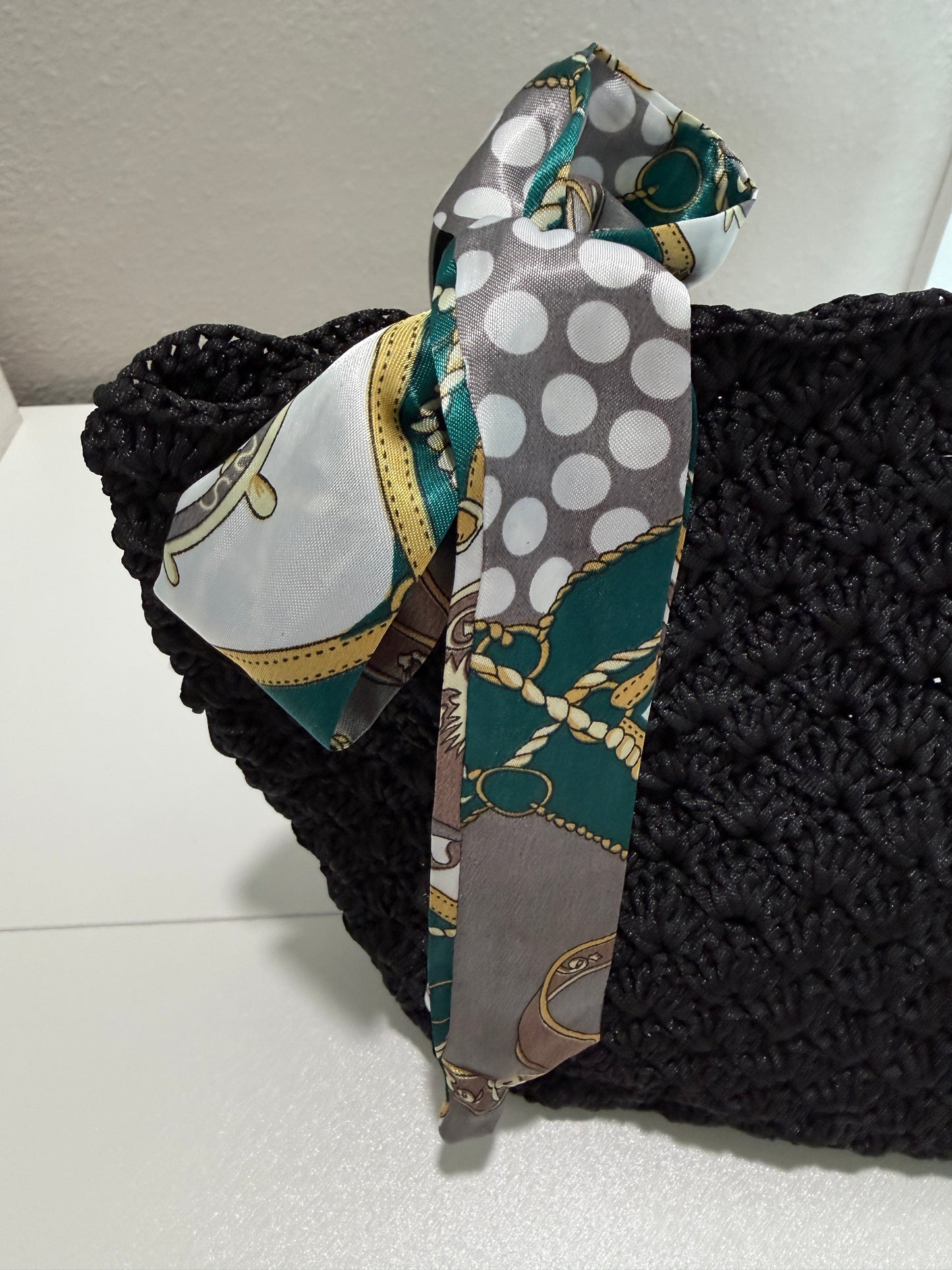 Black crochet purse with patterned fabric scarf on a white background