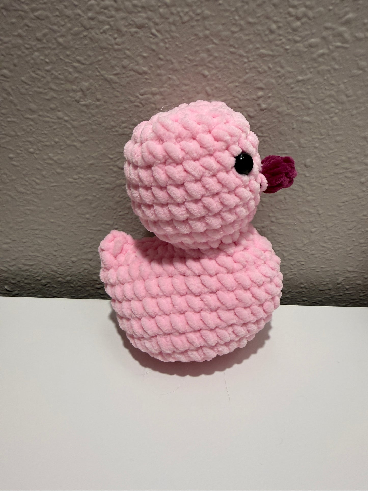 Pink crochet duck against a wall