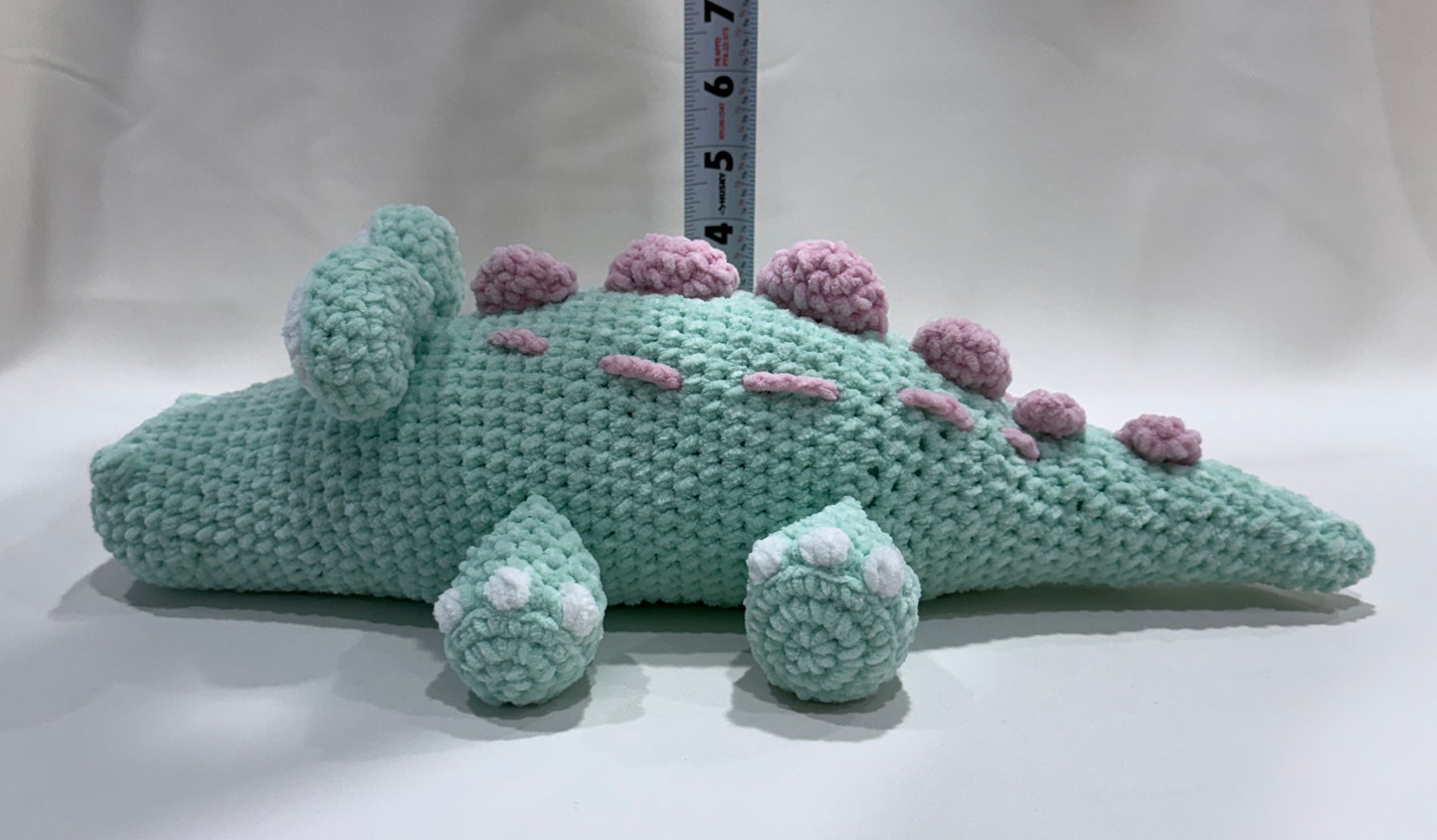 Mint green crocheted crocodile with pink details on a white background