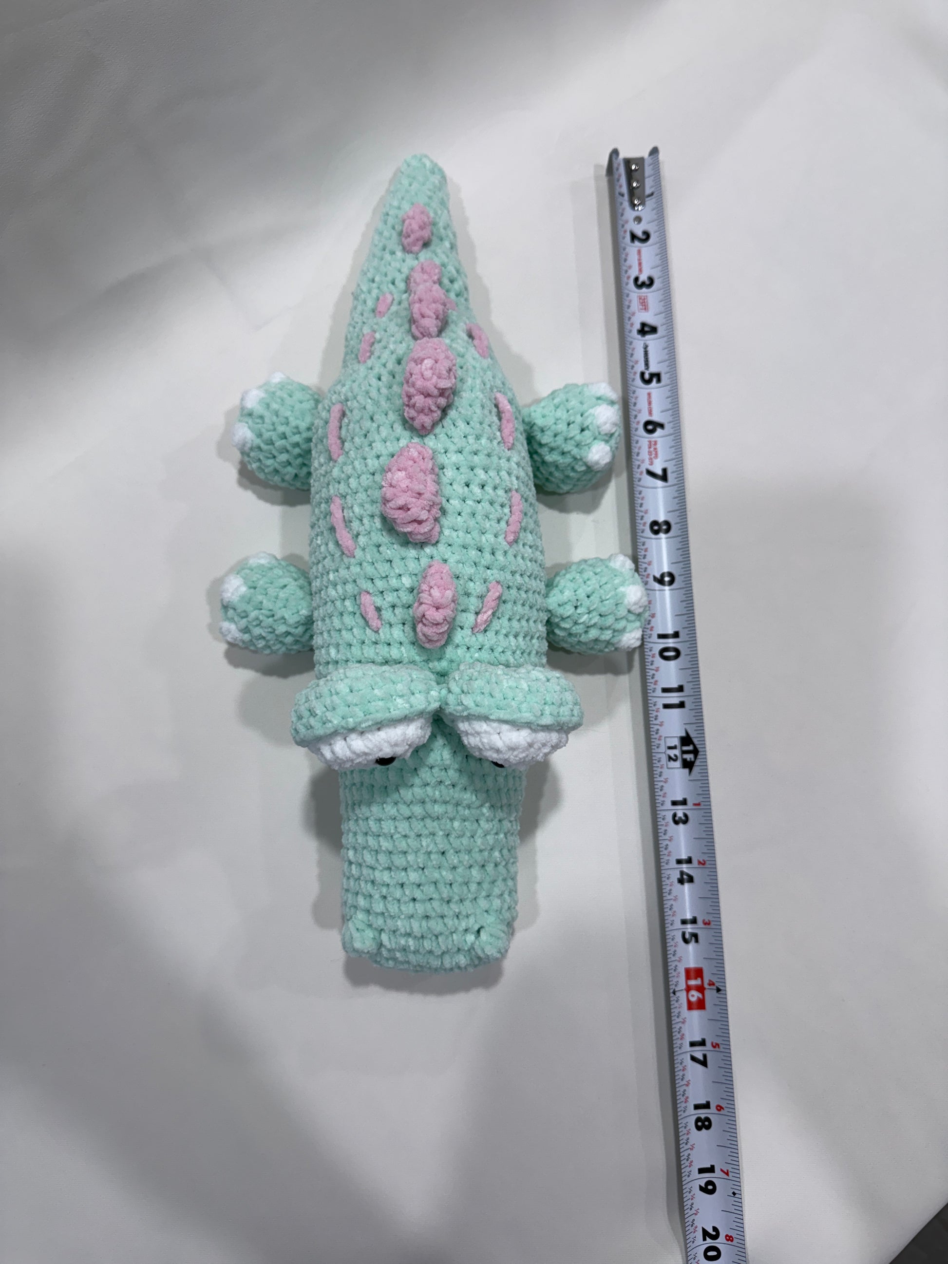 Crocheted crocodile with pink spots on a white background, measured by a ruler.