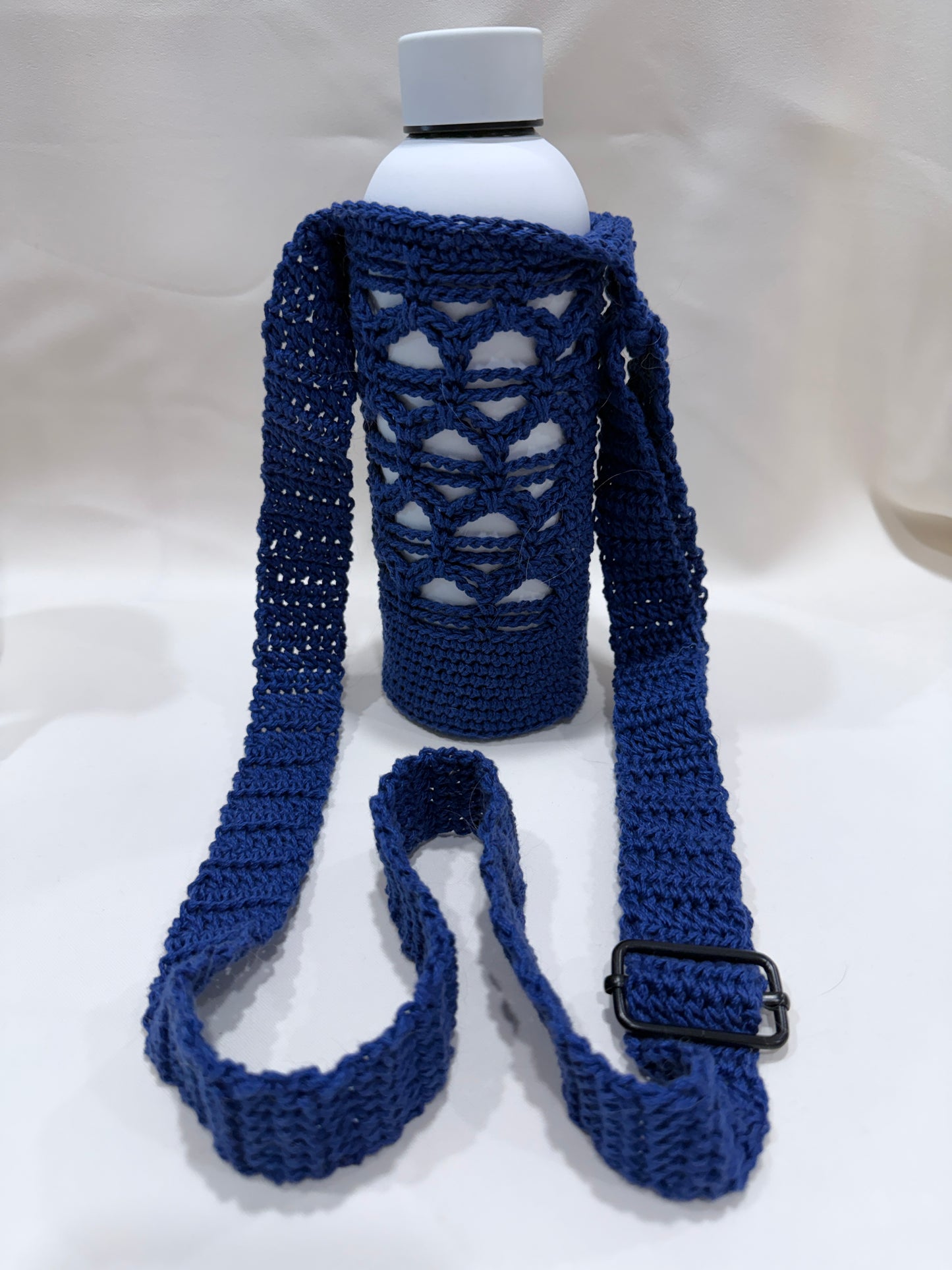 Blue crochet water bottle holder with a buckle and white bottle on a white background