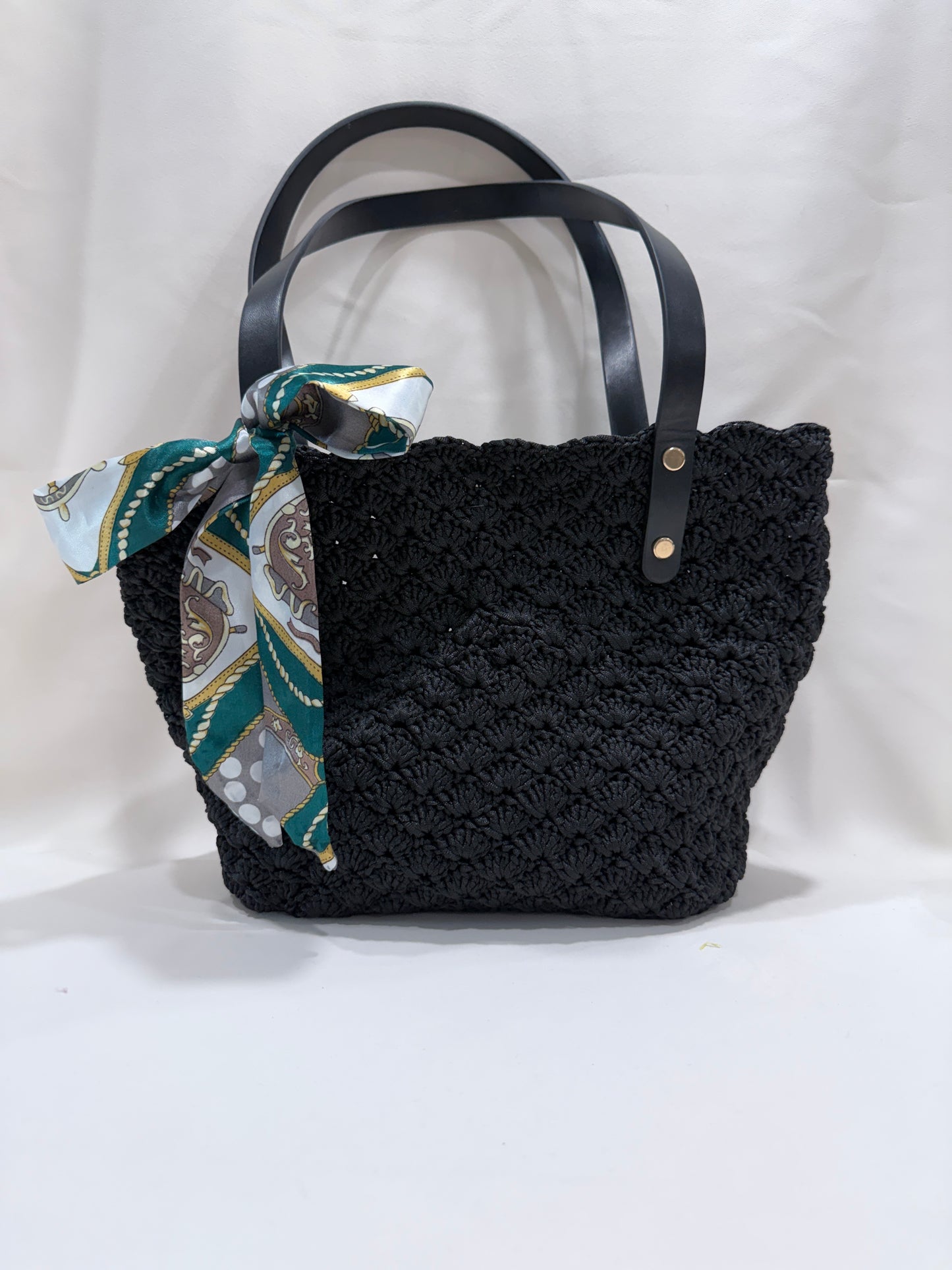 Black crochet handbag with a patterned scarf on a white background