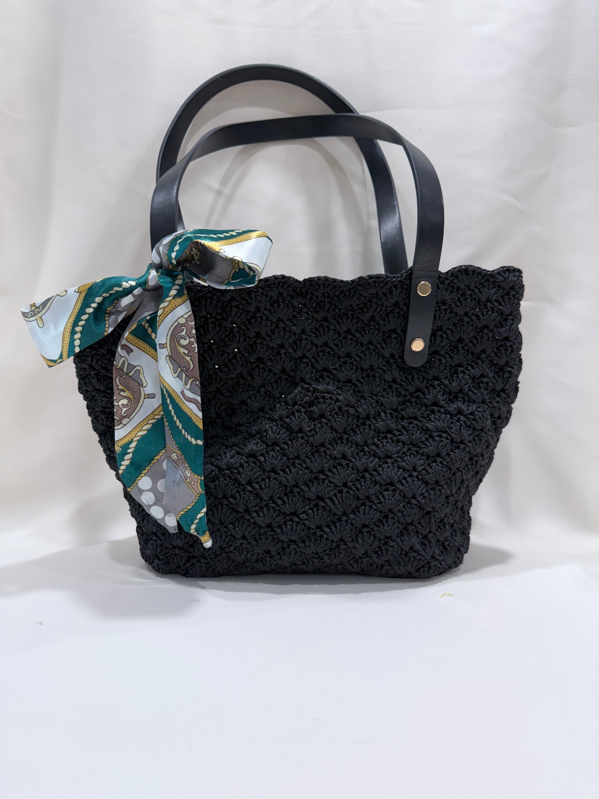 Black crochet handbag with a patterned scarf on a white background