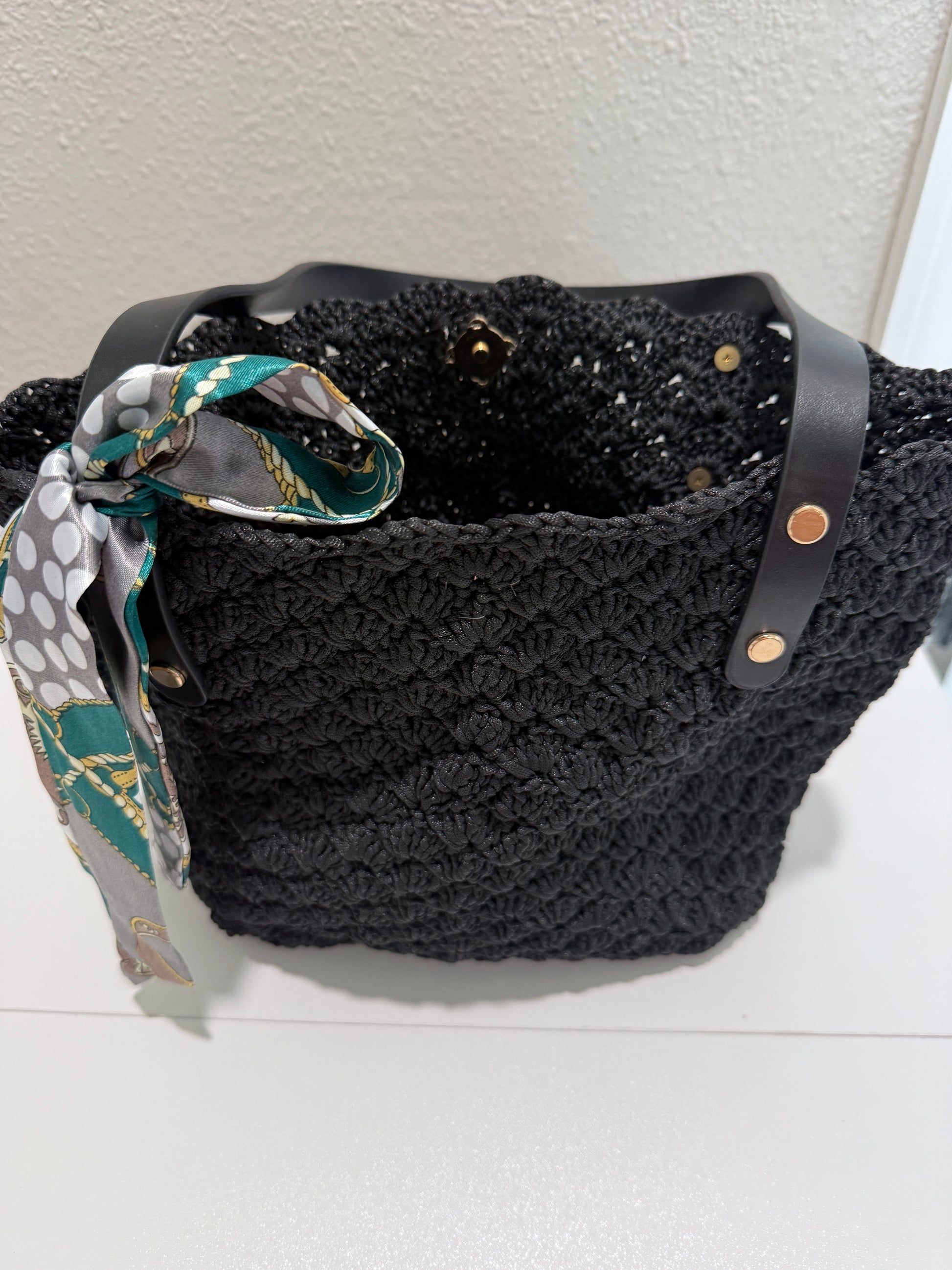 Black crochet handbag with a patterned scarf and clasp in the middle. 