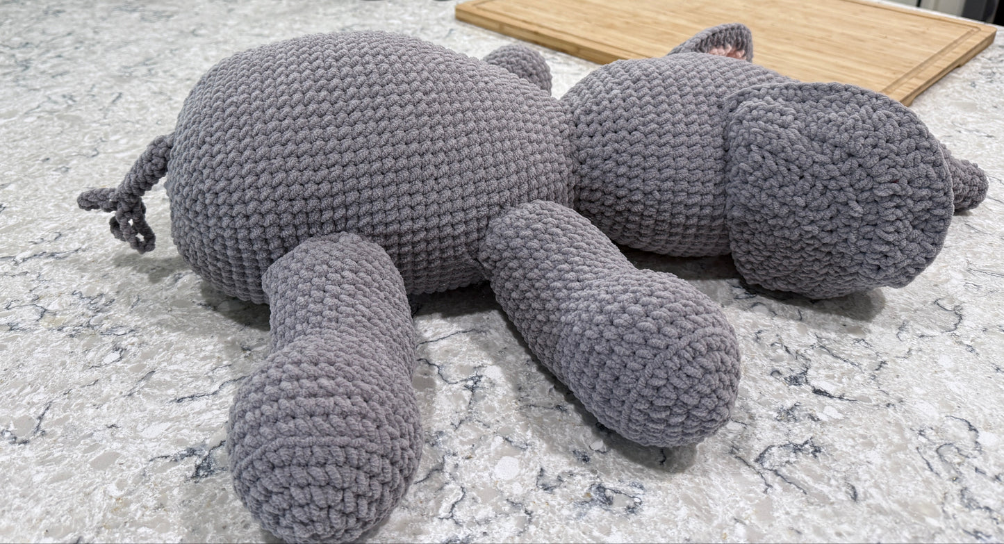 A handmade gray crocheted plush elephant toy lying table displaying its side.