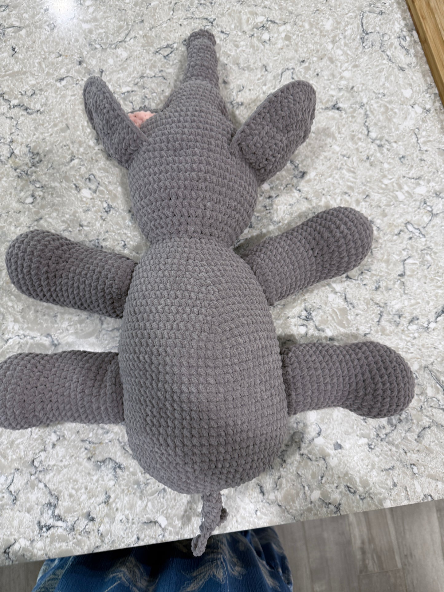 A handmade crocheted gray spider plush toy lying on a white and gray speckled granite countertop.