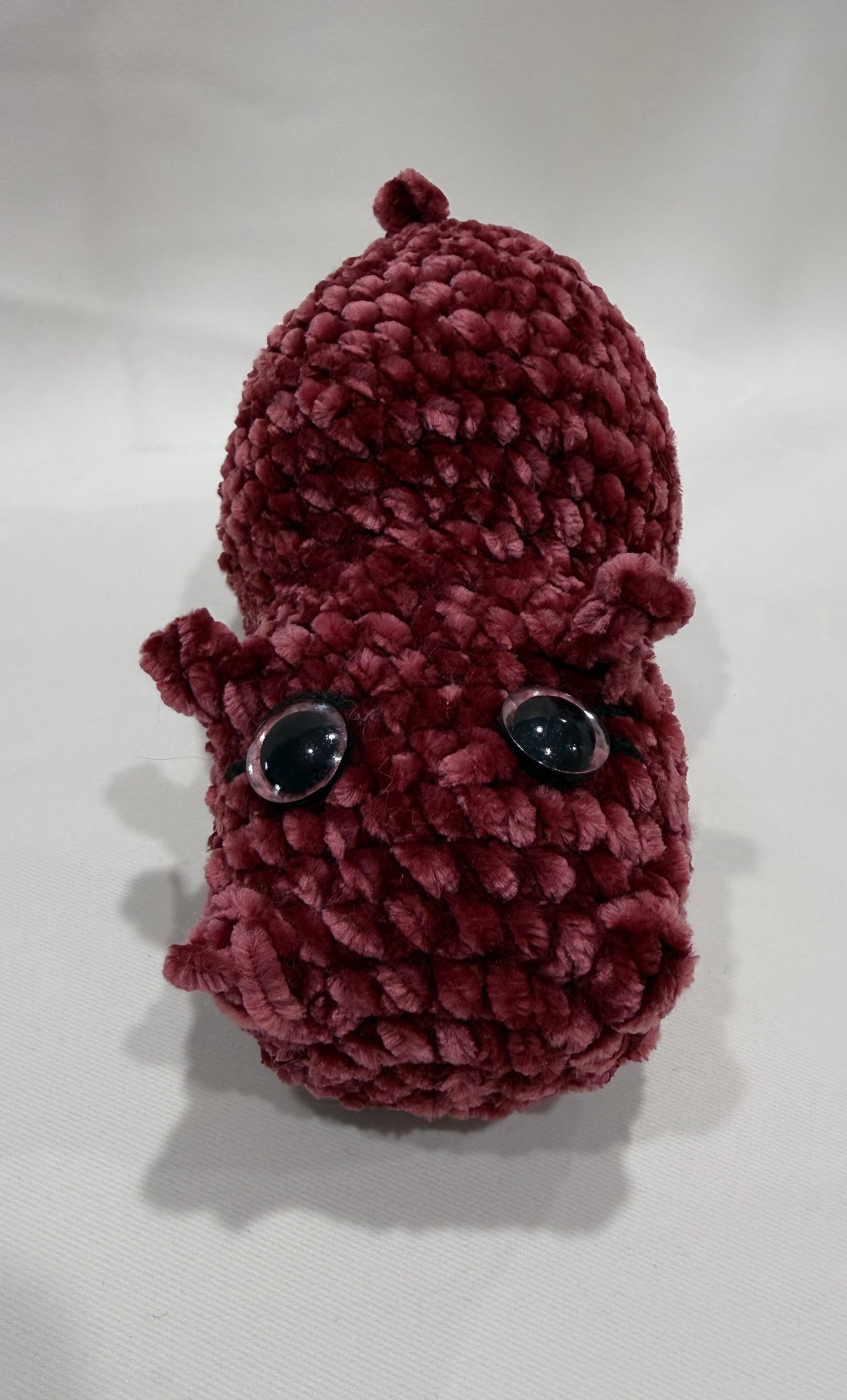 Maroon crochet hippo with black eyes on a white background