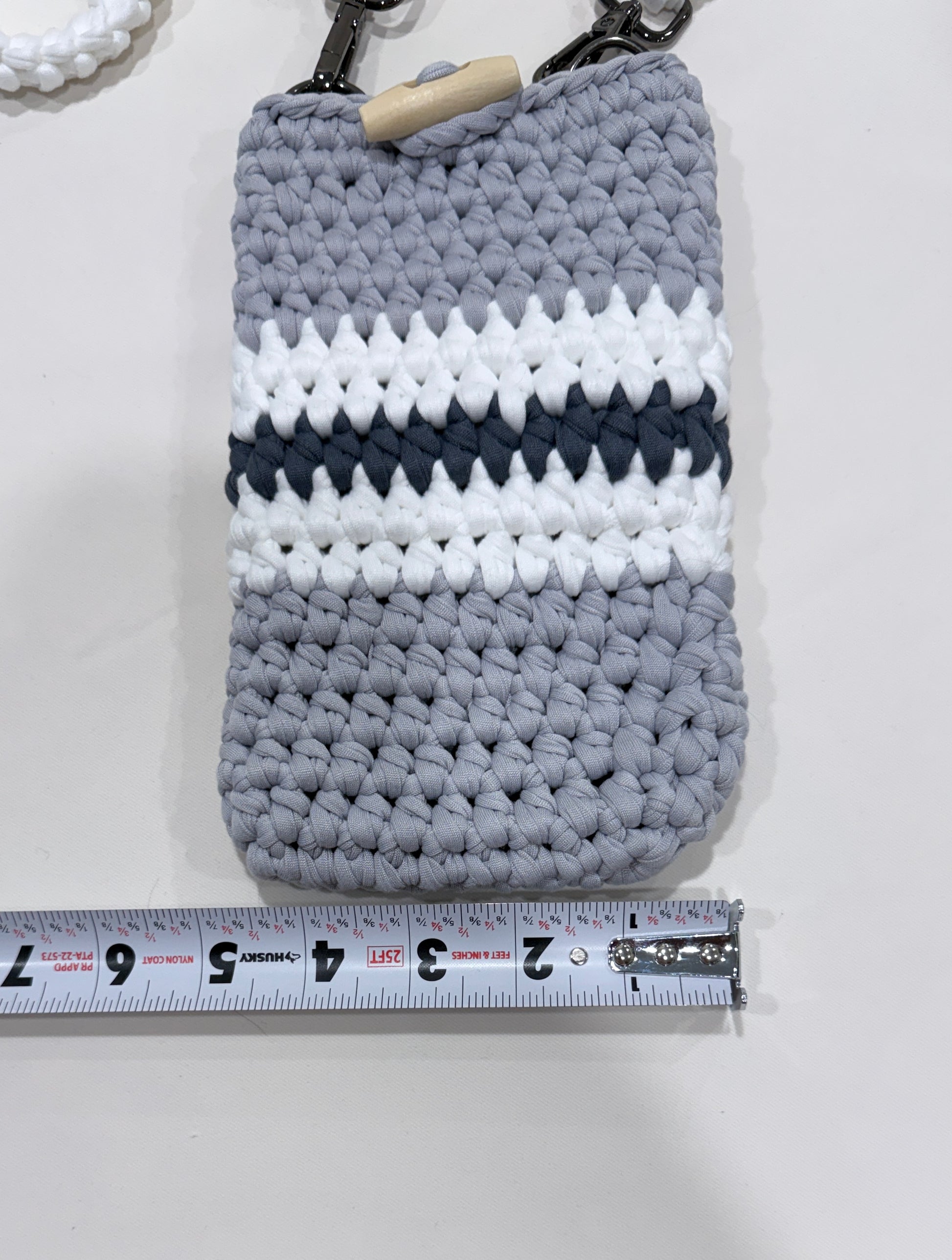 Crocheted pouch with gray, white, and navy pattern next to a ruler for size reference.