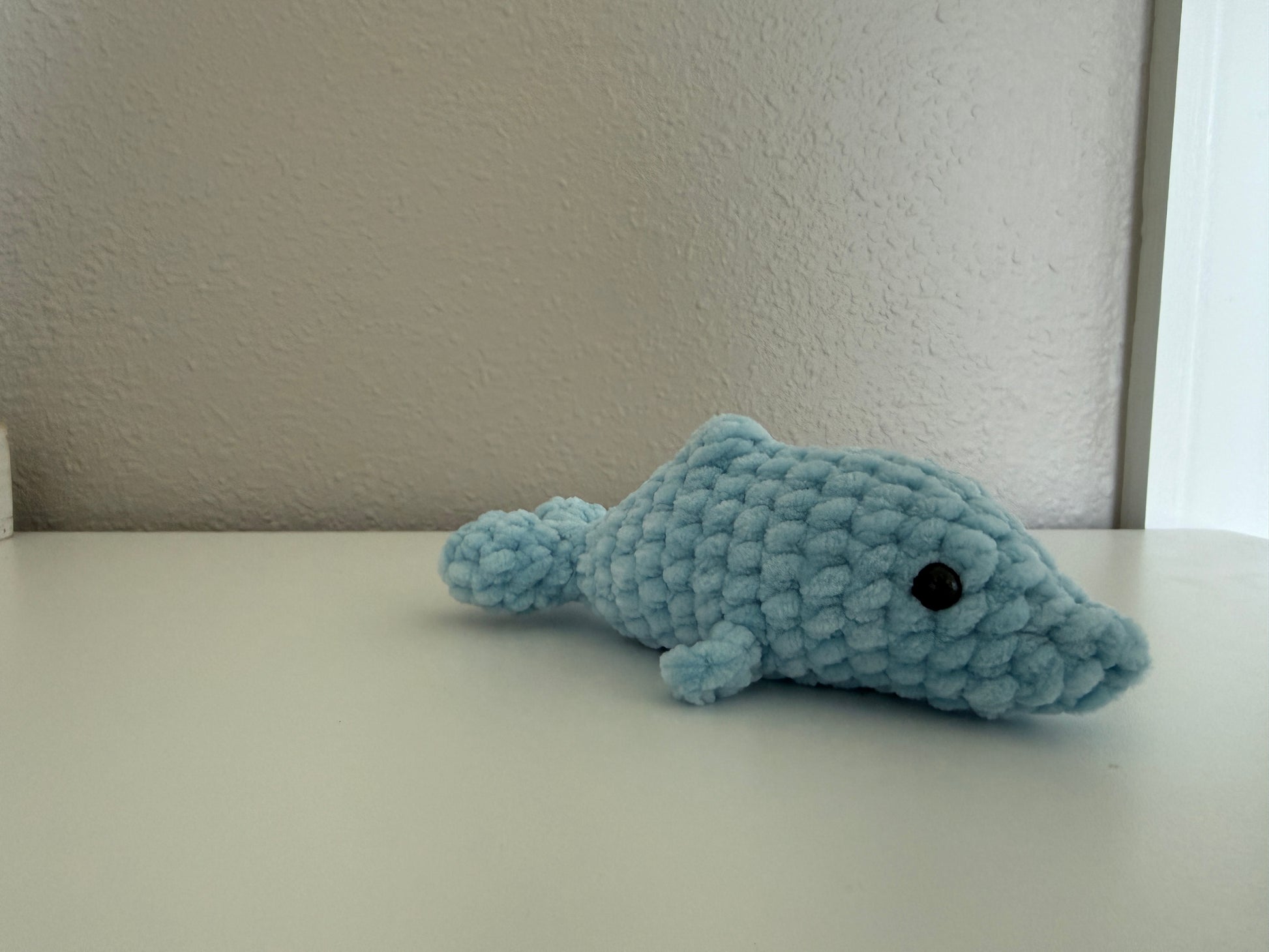 Blue crochet dolphin on a white surface with a neutral background