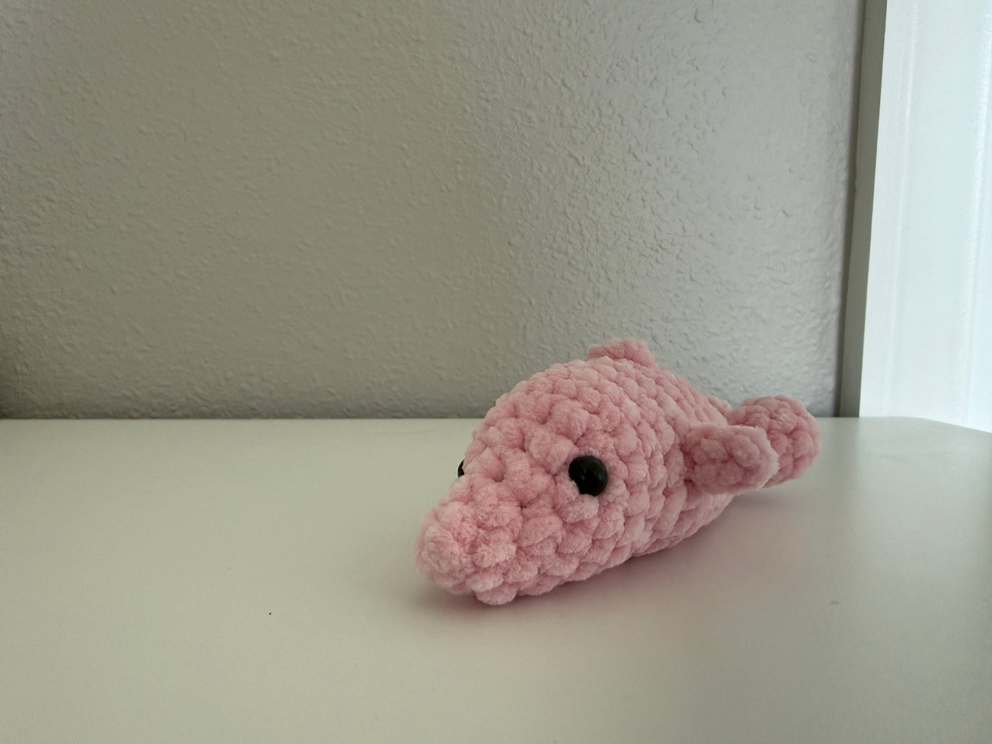 Pink crochet dolphin on a white surface with a neutral background