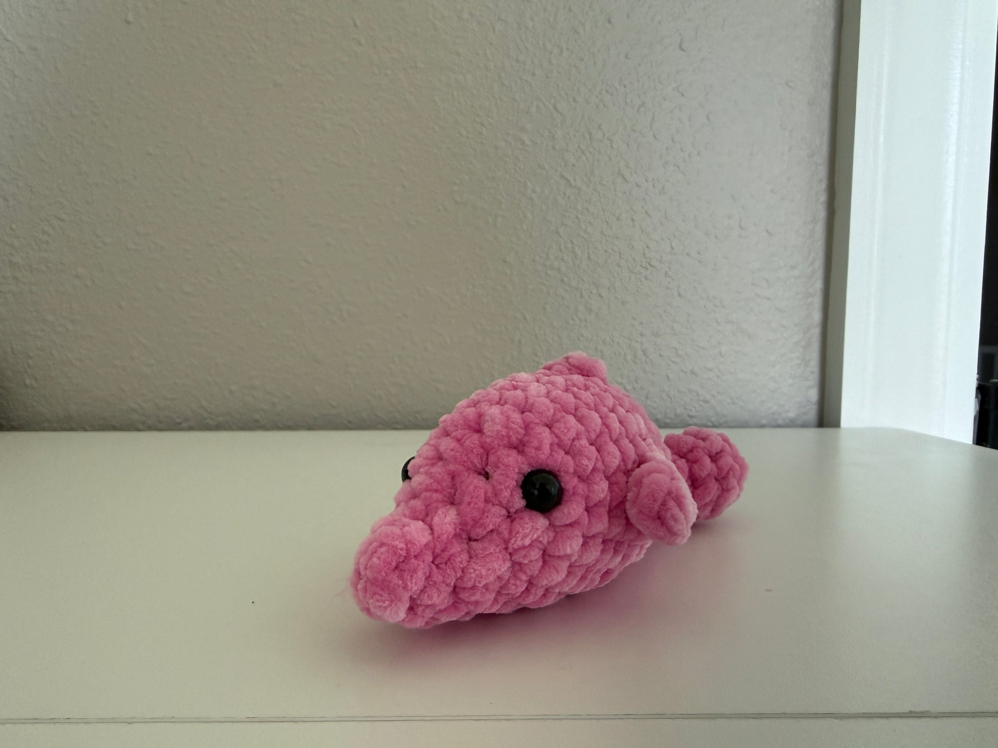 Pink crochet dolphin on a white surface with a neutral background