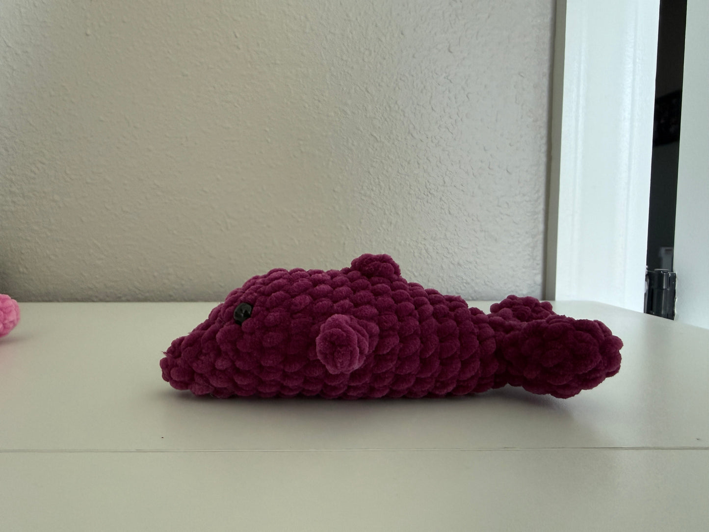 Purple crochet dolphin on a white surface with a neutral background