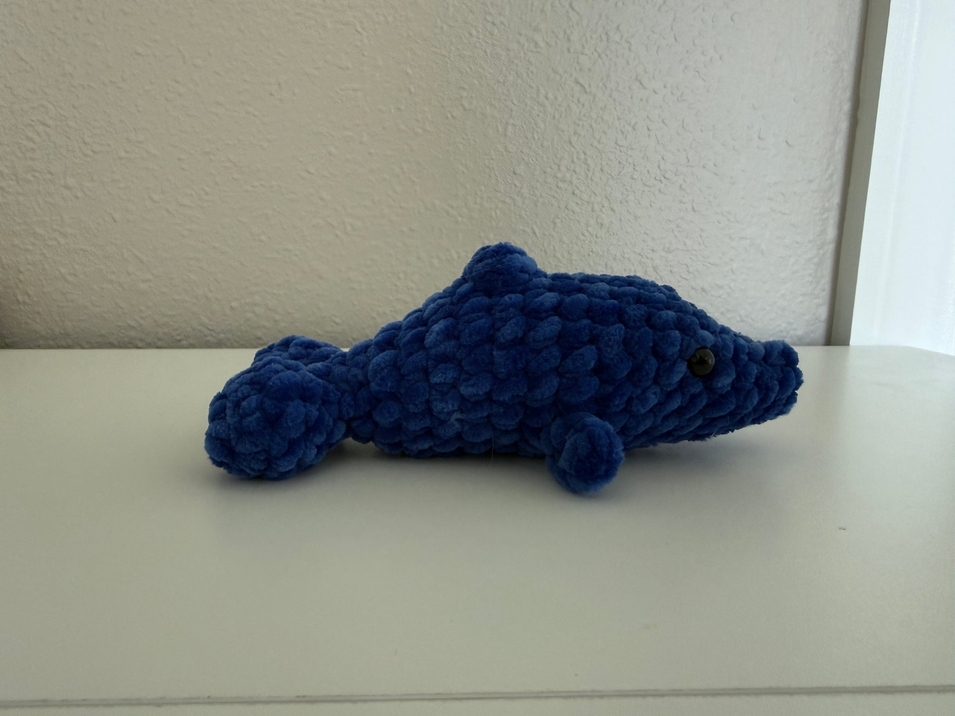 Blue crochet dolphin on a white surface with a neutral background