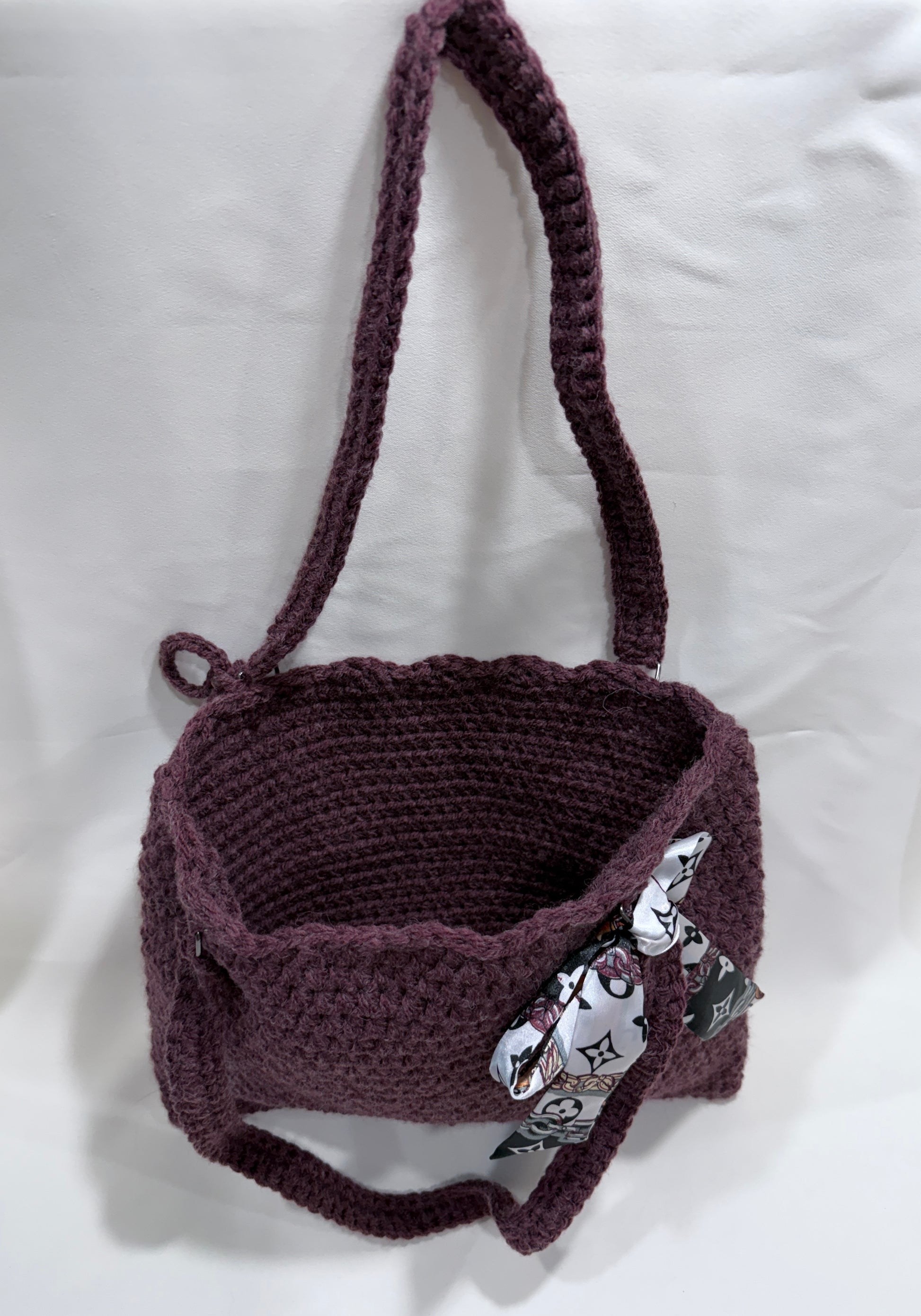 Interior view of wine-colored crocheted handbag with decorative scarf on a white background