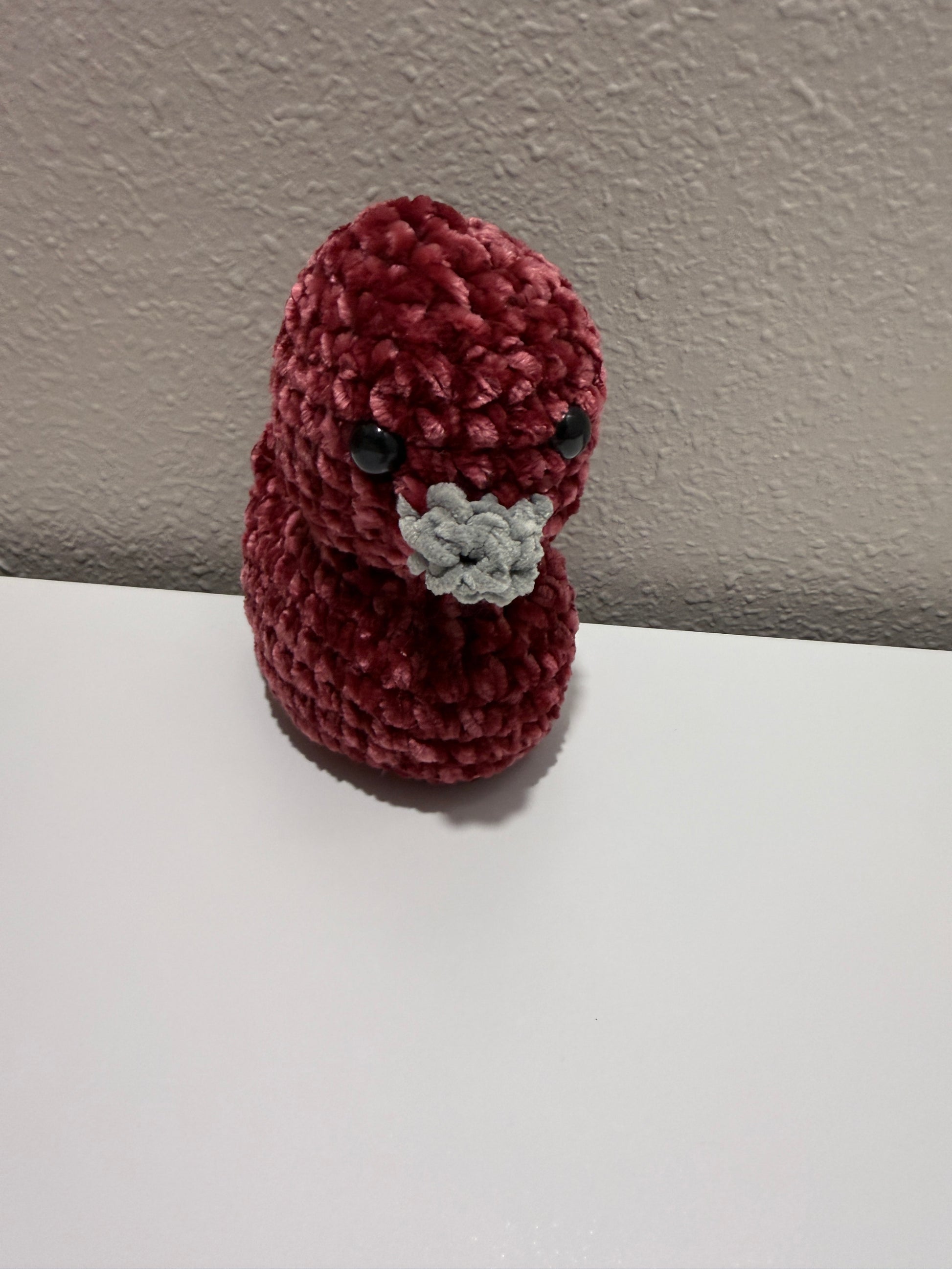 Small red crocheted duck on a neutral background
