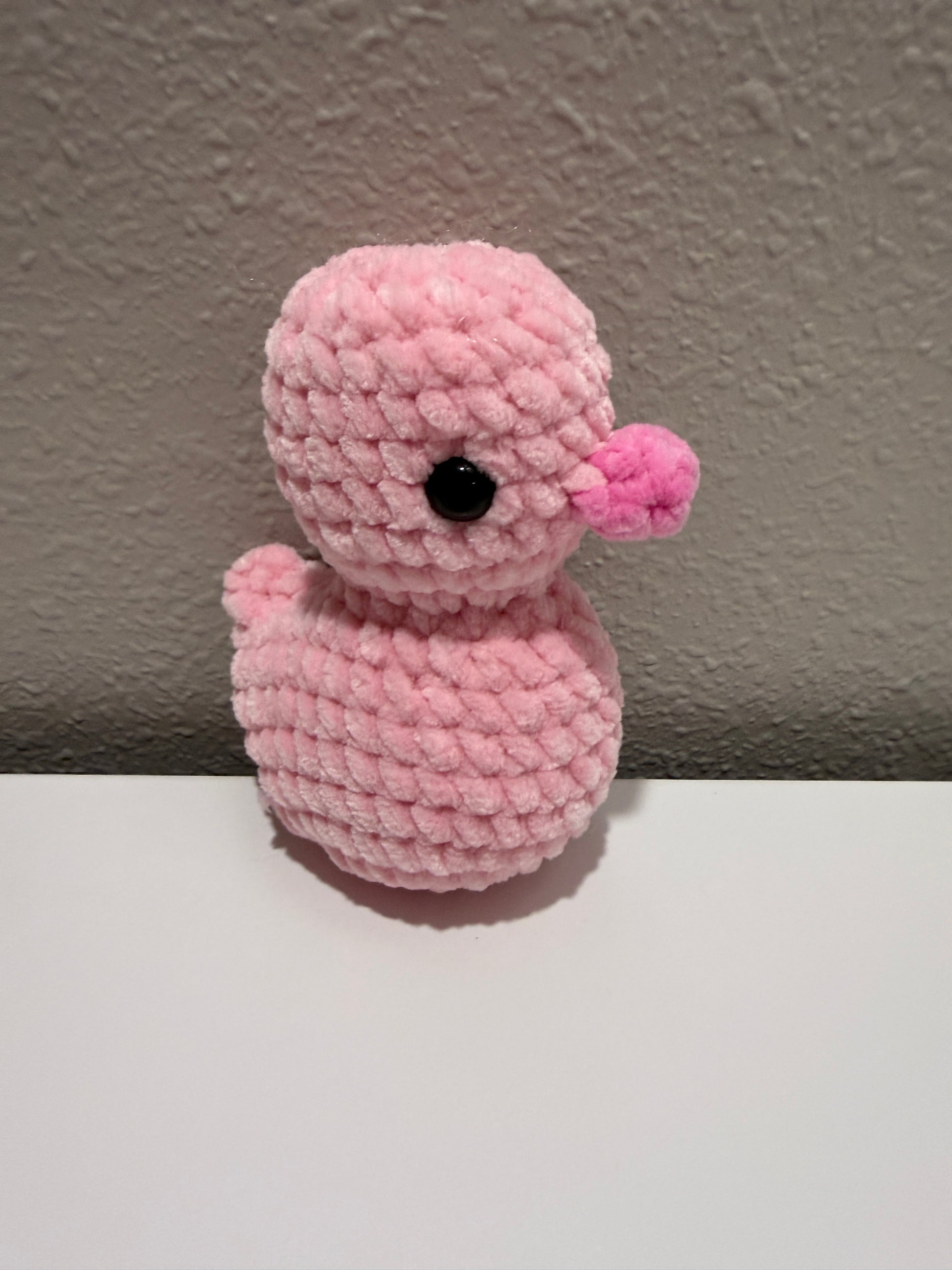Pink crochet duck on a neutral wall.