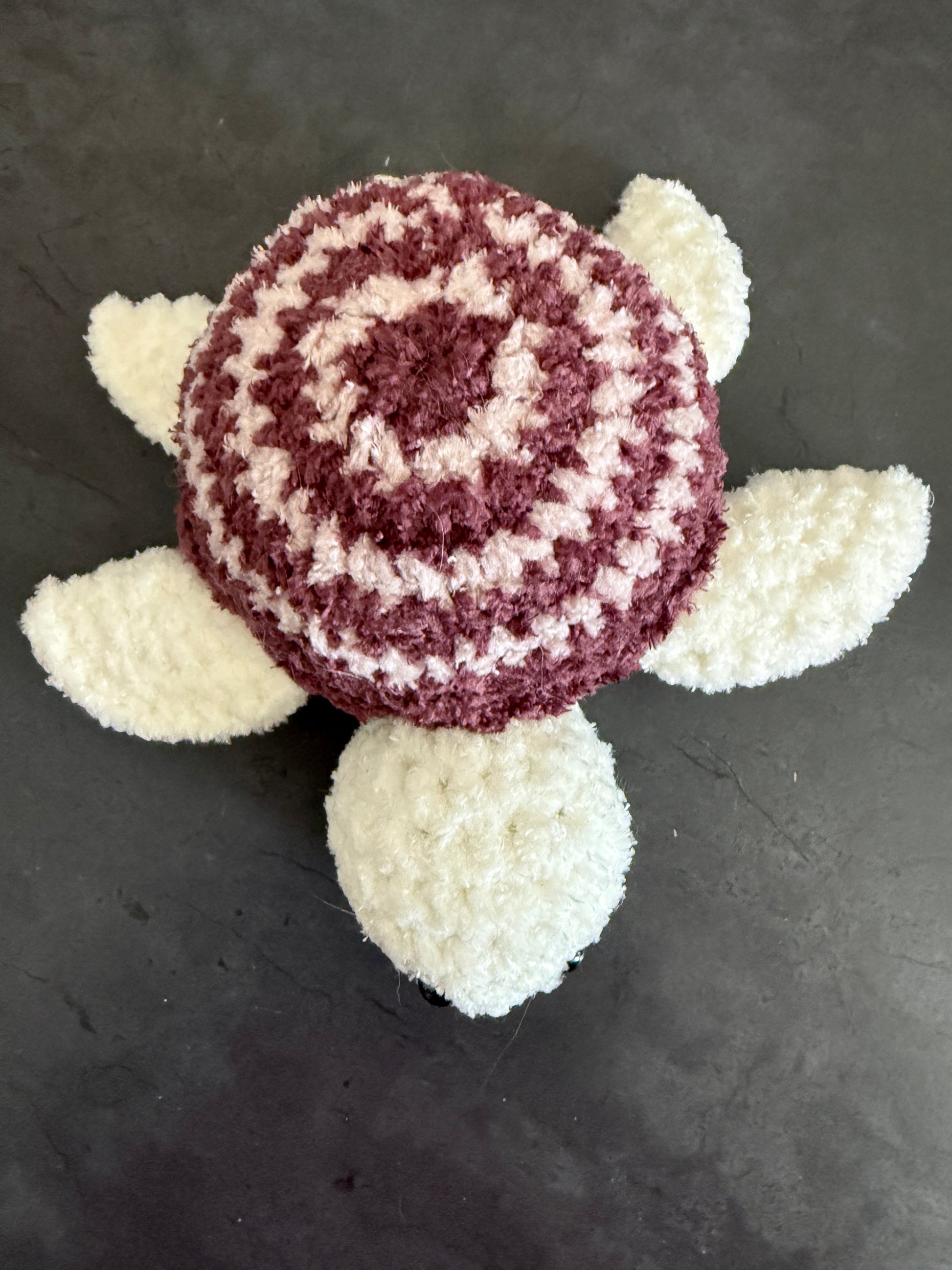 Crocheted turtle with white shell and red body on a dark background