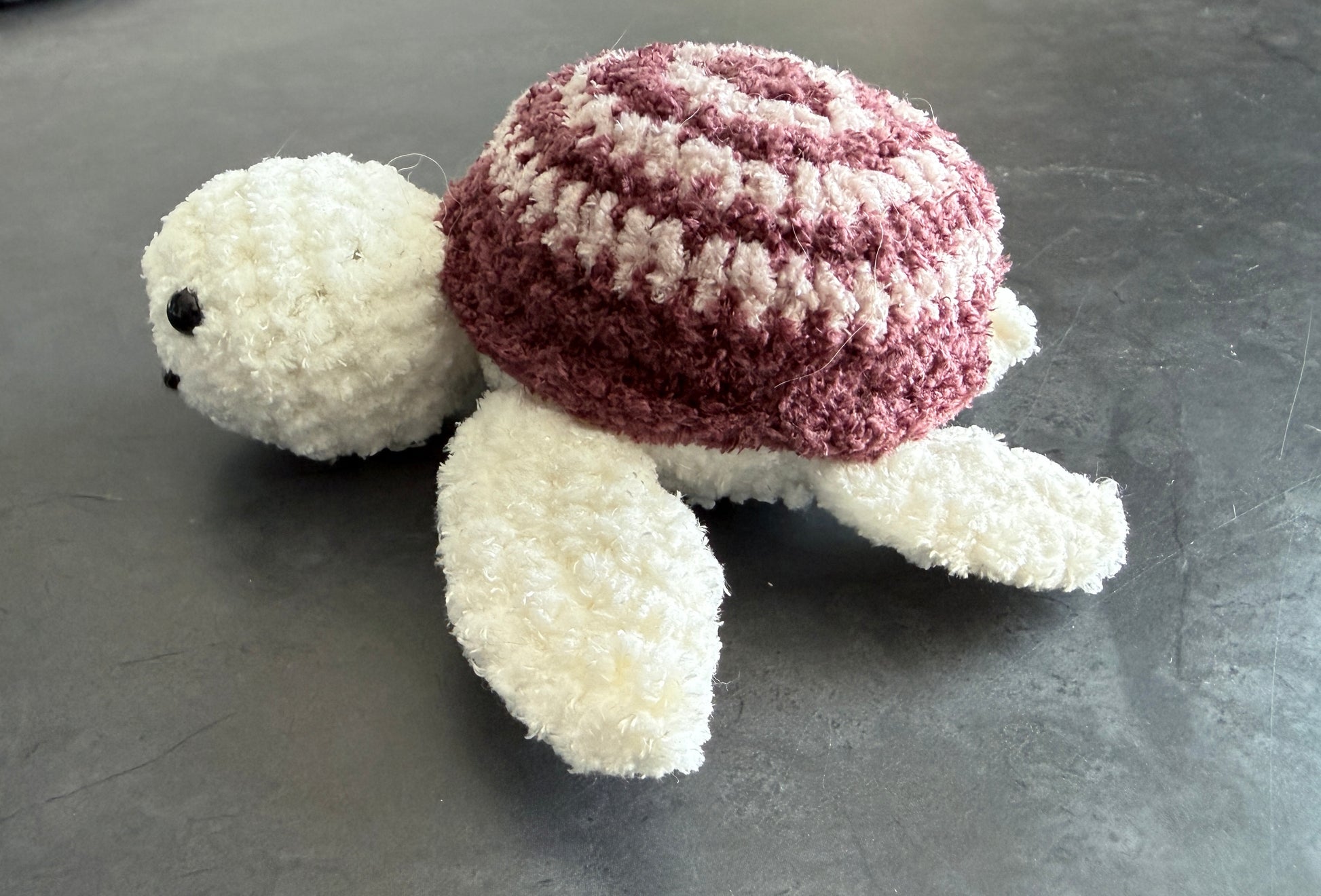 Crocheted turtle with a striped shell on a gray surface