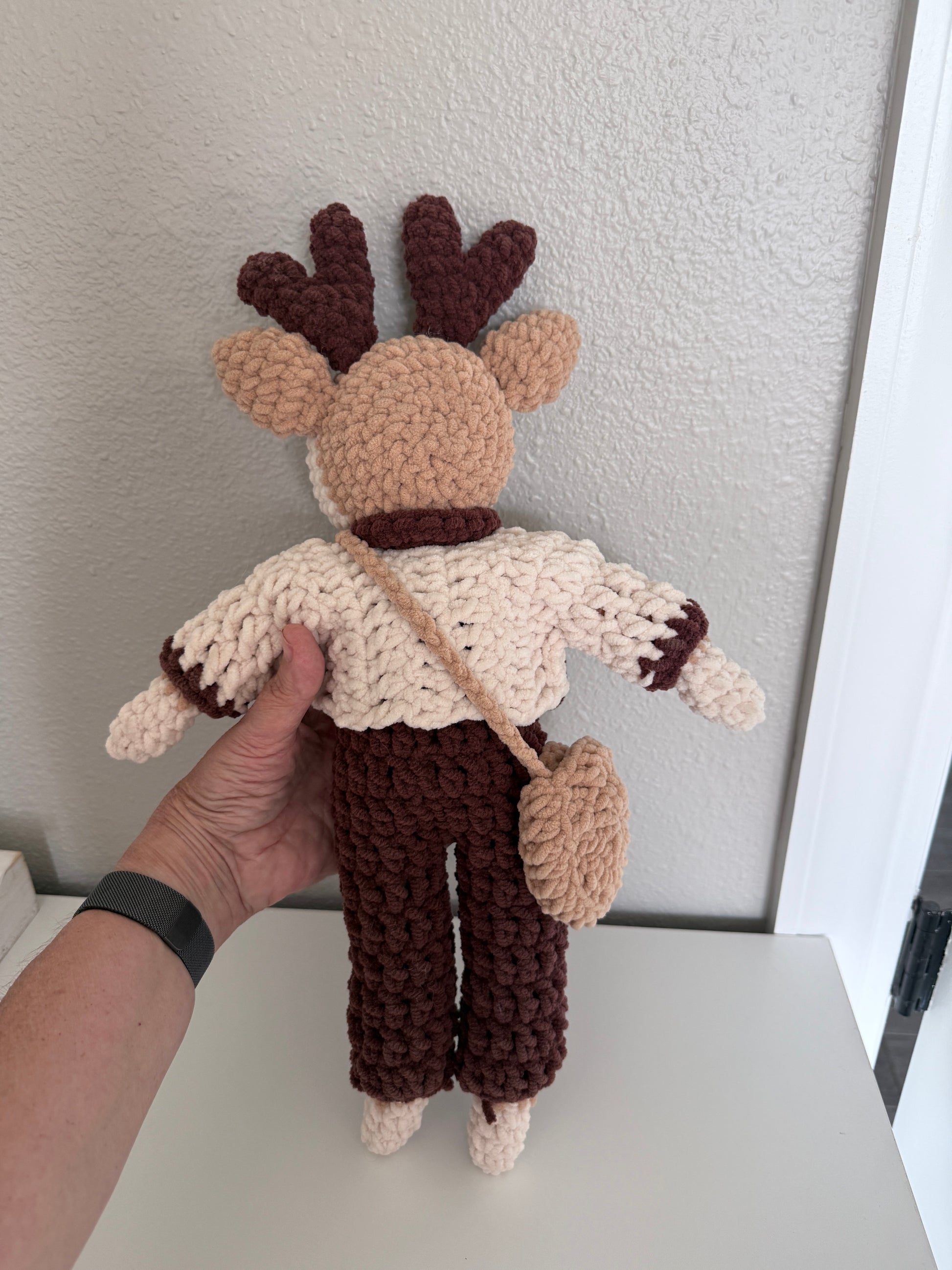 Hand holding a crochet reindeer against a light background