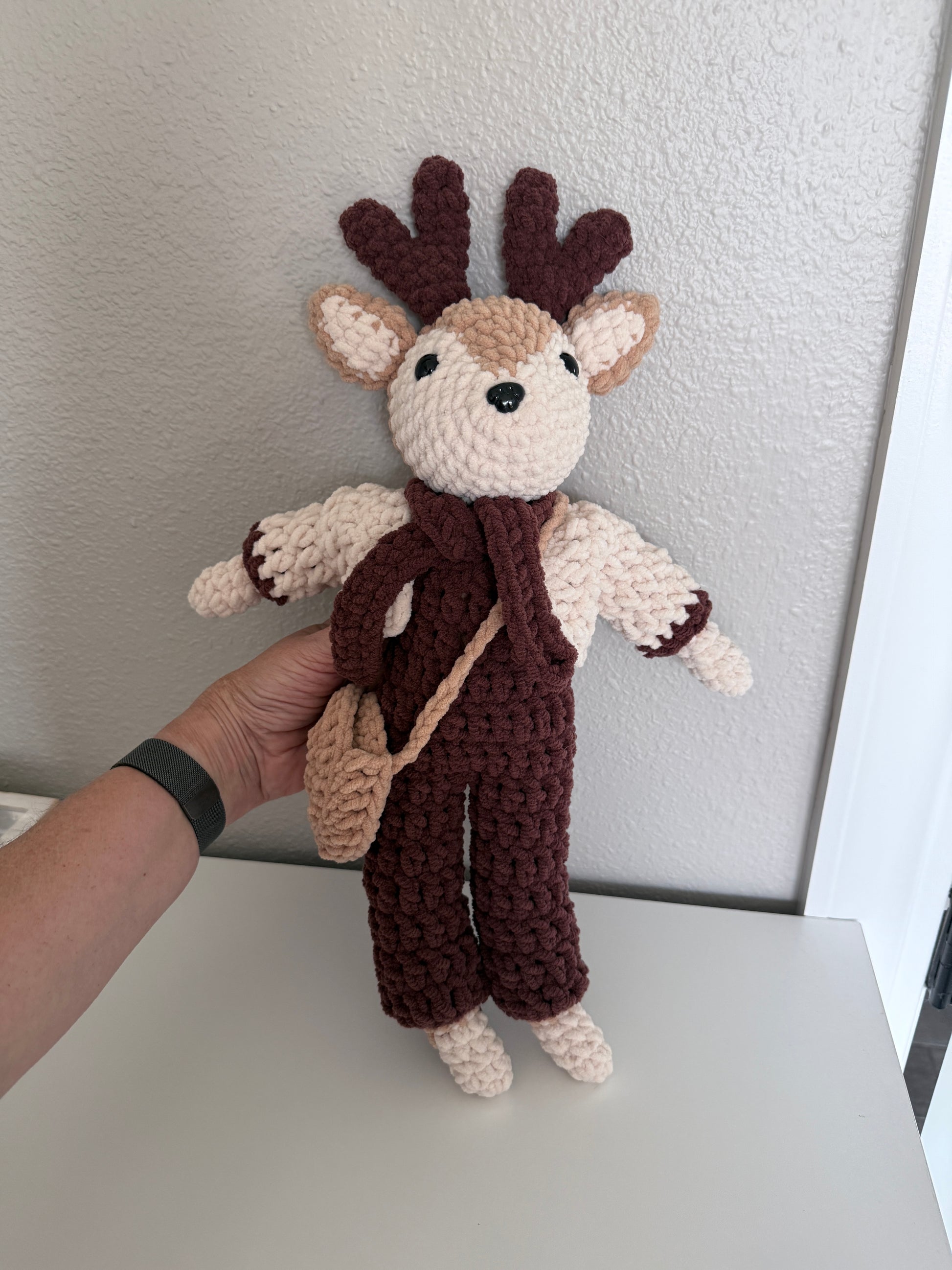 Hand holding a crocheted deer against a plain background