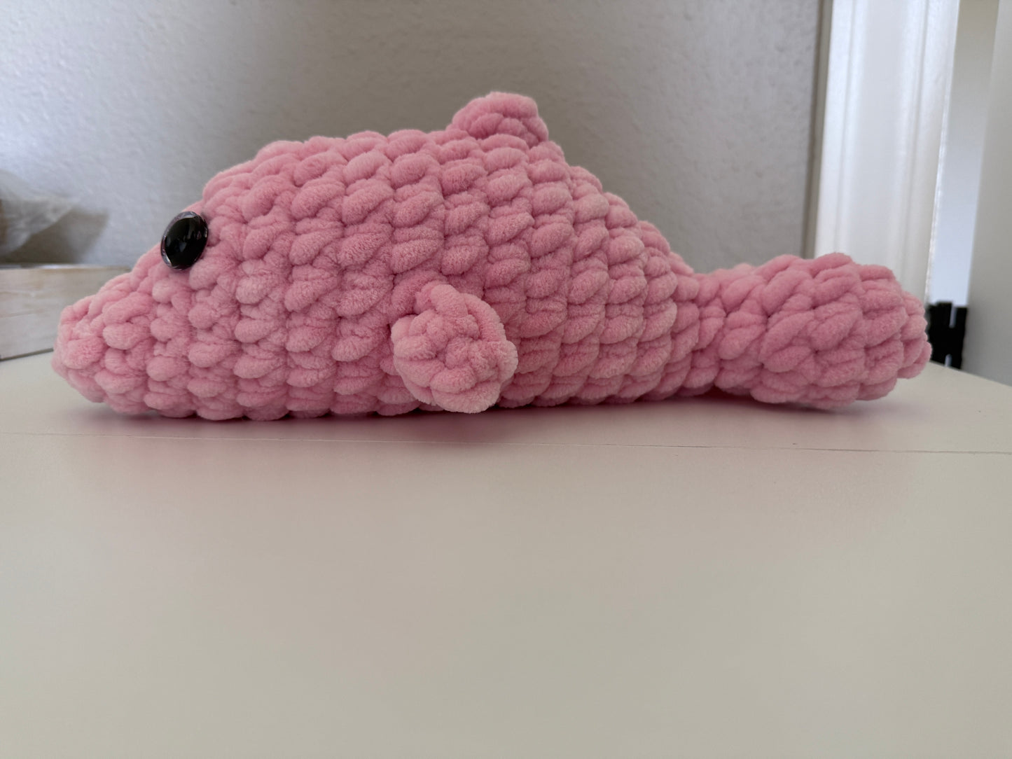 Pink crochet dolphin toy on a white surface