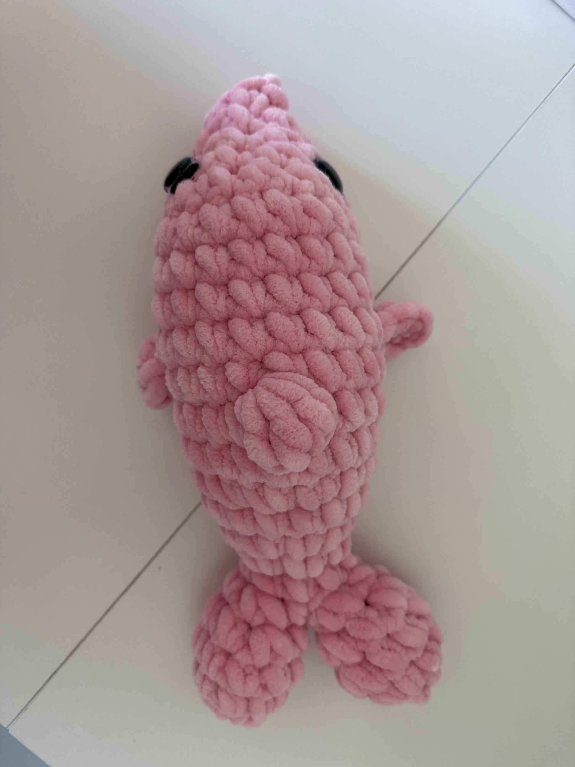 Top view of a pink crochet dolphin on a white background