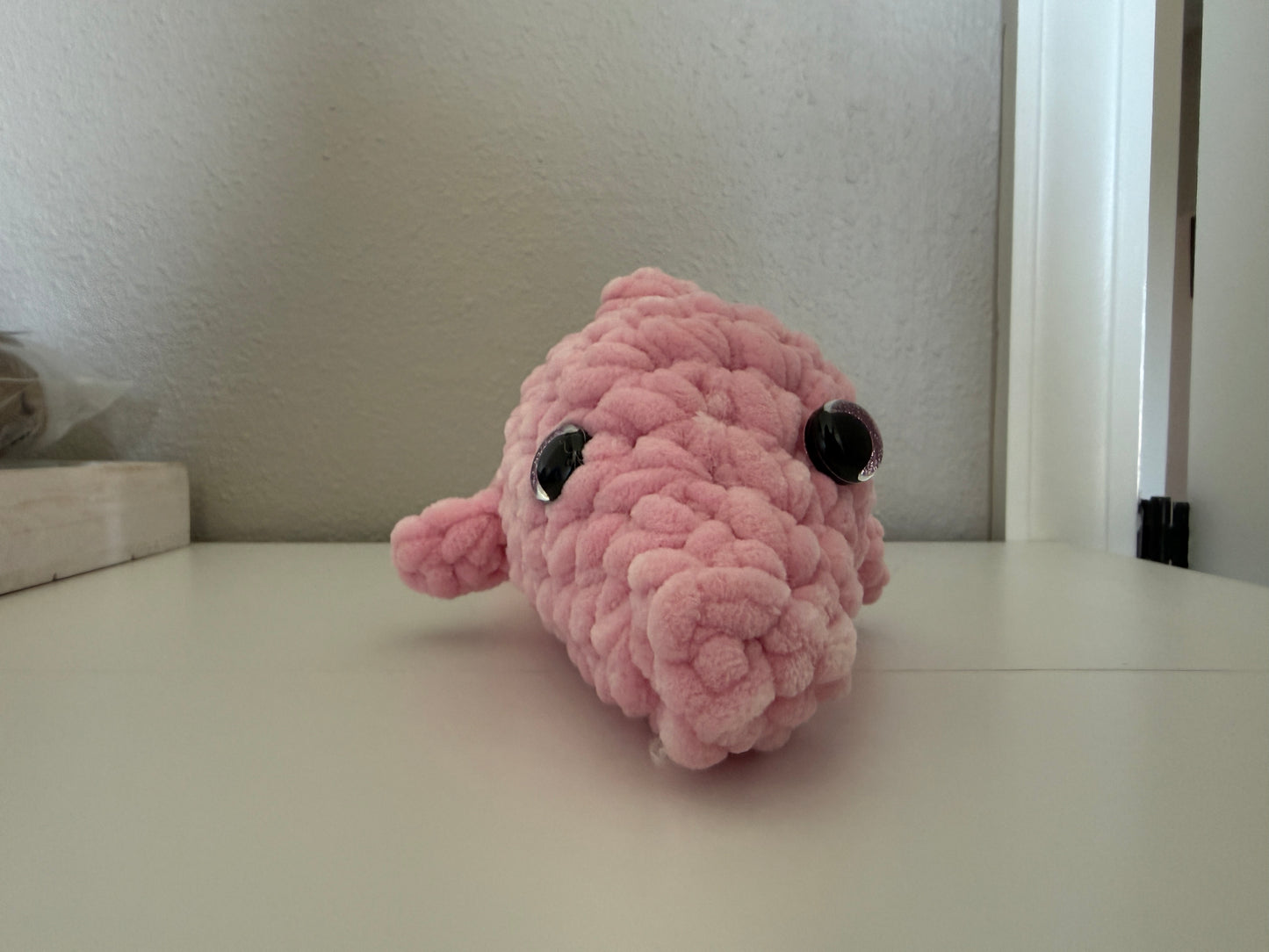 Pink plush dolphin on a white surface with a neutral background