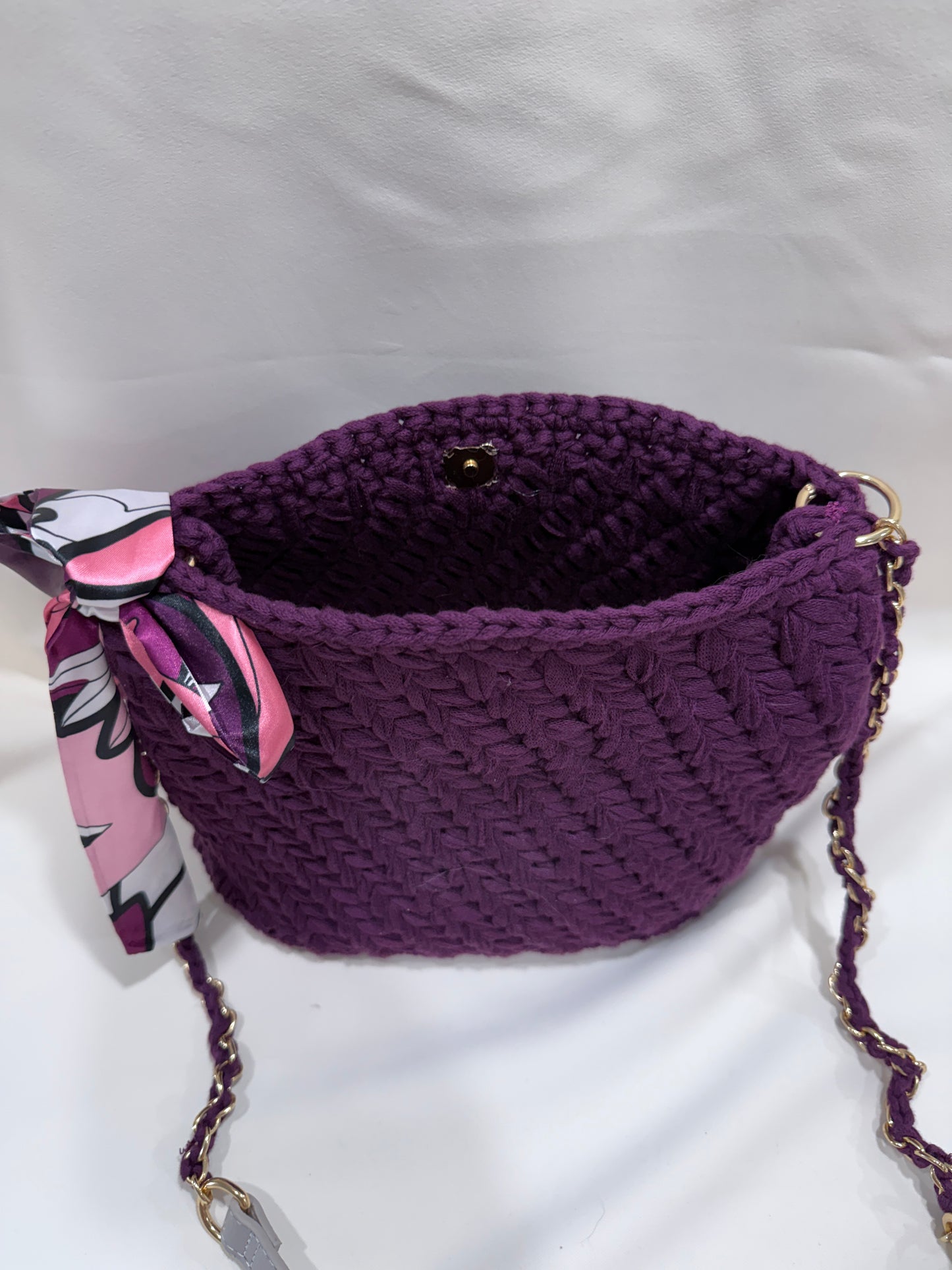 Plum crocheted handbag with floral scarf and patterned strap on a white background