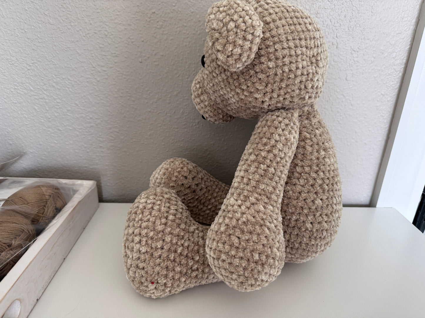 Crochet teddy bear on a white surface with yarn in the background