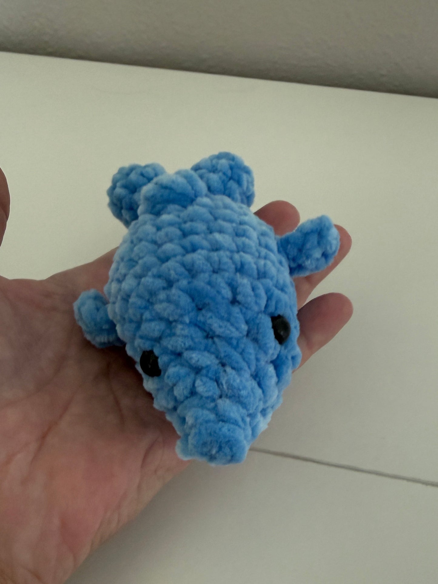 Blue crocheted dolphin held in a hand against a neutral background