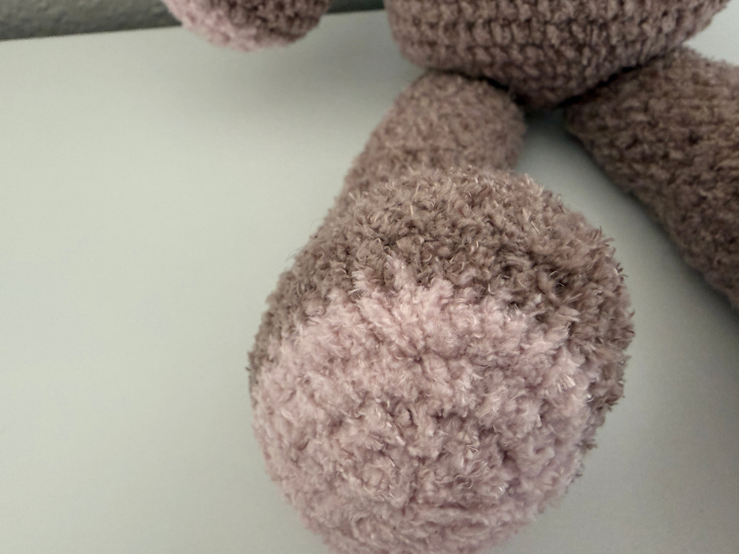 Close-up of a fluffy, brown crochet teddy bear leg on a light gray surface