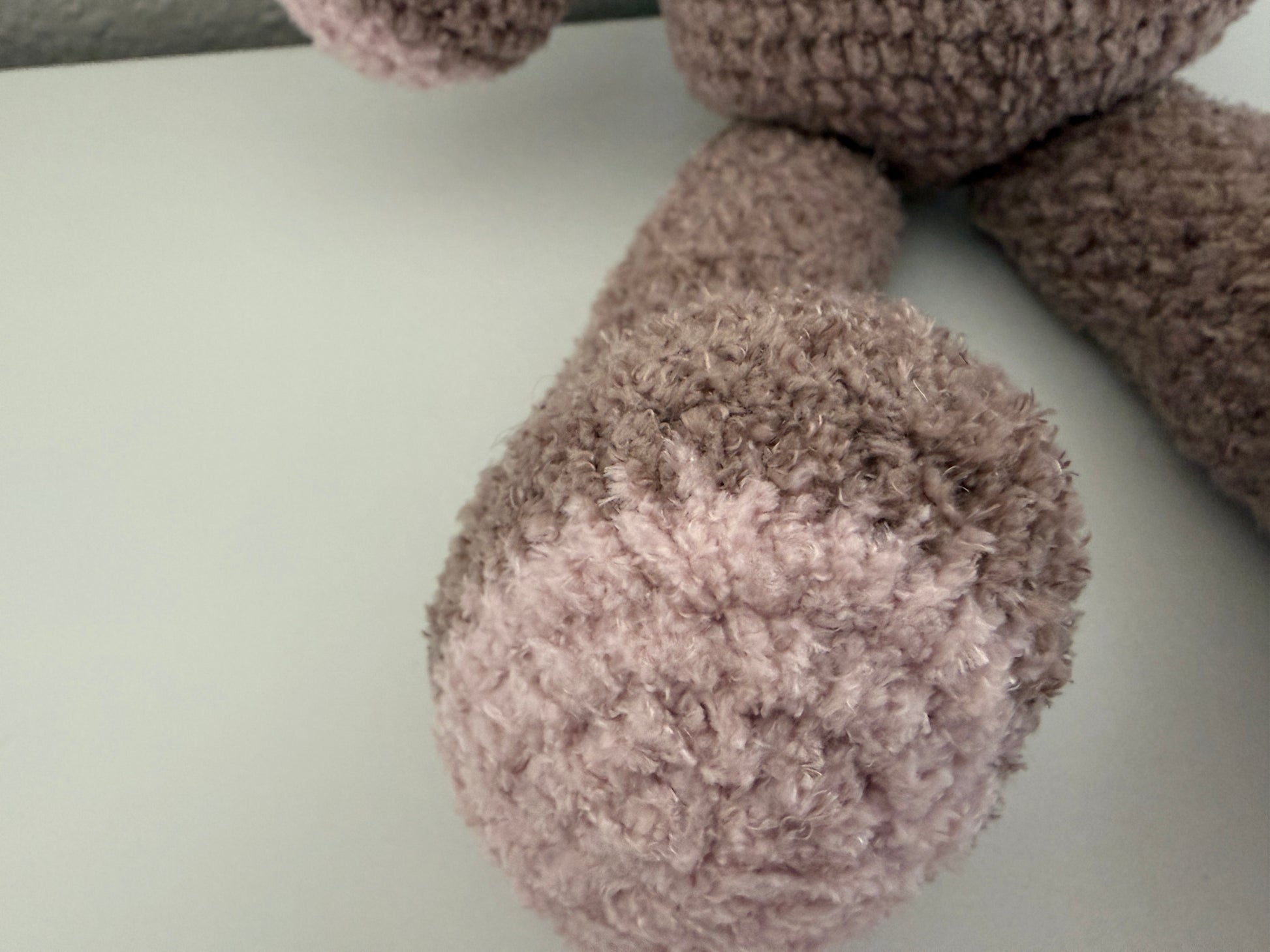 Close-up of a fluffy, brown crochet teddy bear leg on a light gray surface