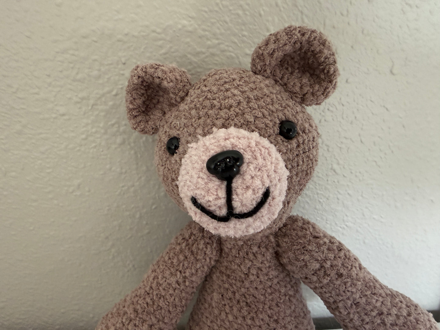 Corchet brown teddy bear against a plain wall